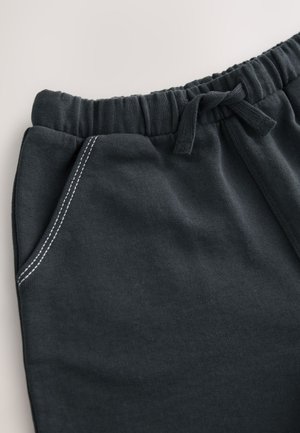 Mørkegrå joggingbukser med ribbet taljebånd, elastisk snørre, sidelomme og kontrasterende hvide sømdetaljer. Blød stoftekstur.