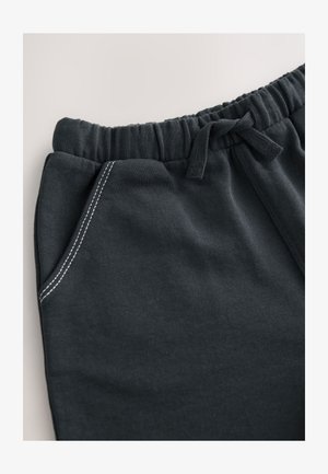 Tmavomosivé teplákové nohavice s rebrovaným pásom, elastickým sťahovacím šnúrkou, bočným vreckom a kontrastným bielym prešitím. Mäkká textúra materiálu.
