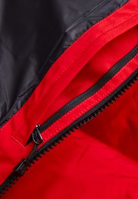 Röd och svart zippered jacka med en slät, glänsande yta; insidan har en kontrasterande röd foder och en robust svart dragkedja.