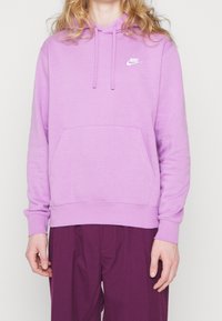 Ljuslila Nike-hoodie med framfickor, dragsko på huvan och vit logga på bröstet; mjukt tyg, avslappnad passform.