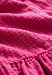Tissu à texture douce en rose vif avec des parties rassemblées et froissées créant une surface tactile et irrégulière.