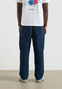 Granatowe, luźne spodnie o gładkiej fakturze z dwiema tylnymi kieszeniami, połączone z białą koszulką z grafiką o kolorowym wzorze.