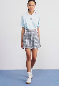 Polo de culoare albastru deschis, cu mânecă scurtă și guler, asortat cu o fustă plisată gri cu carouri. Modelul poartă adidași albi și șosete.
