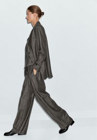 Abito grigio a righe con giacca morbida e pantaloni a gamba larga. Le scarpe nere completano l'outfit. Fondale semplice.
