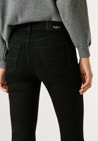 Vaqueros de mezclilla negra con un diseño ajustado, que cuentan con bolsillos traseros y detalles de costura sutiles. Combinados con un suéter de punto gris.