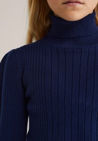 Sötétkék bordázott garbós pulóver texturált kötött anyagból. Függőleges csíkokkal és a gallér, valamint a ujjak körüli testhezálló dizájnnal rendelkezik.