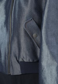 Kurtka bombowiec z denimu w ciemnoniebieskim kolorze, z metalowym suwakiem, ściągaczami na rękawach oraz boczną kieszenią z czarnym zatrzaskiem.