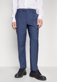 Blaue maßgeschneiderte Hosen aus einem strukturierten Stoff, mit flachem Front und schlanker Passform, kombiniert mit schwarzen Schnürschuhen.