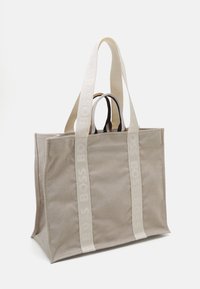 Borsa a tracolla in tela color beige chiaro con due spallacci grossi e goffrati color bianco sporco. Design strutturato con bordi rinforzati e interno spazioso.