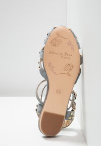 Semelle d'une sandale en daim bleu avec des clous dorés, embossage de rose et de feuille, taille 37, marquée "Alma en Pena España" sur une semelle beige.