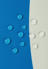 Blau-weißes Textil mit mehreren klaren und blauen Wassertropfen, die in Größe und Muster variieren und glänzende Oberflächen und Texturen zeigen.