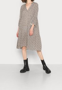 Robe à imprimé floral beige avec un décolleté en V profond, manches longues et jupe à volants. Associée à des bottines noires épaisses.