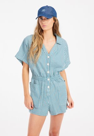 Combinaison rayée en turquoise et blanche, manches courtes, devant à boutons, taille élastique, deux poches latérales, associée à une casquette de baseball en denim.