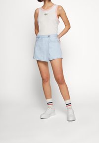 Ljusblå denimkjol med omslagsdesign, tillsammans med en vit linne med rosa kant och en liten grafik, samt vita sneakers.