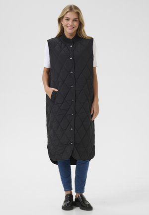 Black quilted sleeveless vest with a stand collar, snap buttons, and side pockets, worn over a white top and paired with blue jeans.
