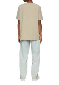 Beige t-shirt met korte mouwen en een relaxed fit, gecombineerd met lichtblauwe wijde jeans. Eenvoudig ontwerp, zonder zichtbare patronen of accenten.