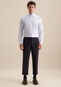 Camicia a righe azzurro chiaro con bottoni abbinata a pantaloni scuri plissettati e scarpe in pelle nera, mostrata su uno sfondo semplice.