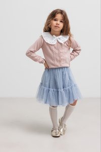 Cardigan lavorato a maglia rosa chiaro con colletto in pizzo, abbinato a una gonna in tulle blu a strati e calze bianche fino al ginocchio. Le scarpe dorate completano il look.