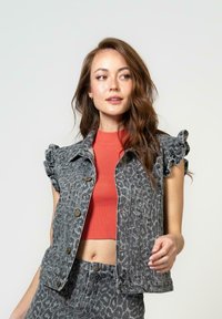Grå leopardmønstrete denimvest med puffede ermer, paret med en tettsittende rød ribbestrikket kort topp. Glatt tekstur, metalliske knapper og en kort design.