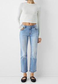 Vit långärmad croppad topp tillsammans med ljusblå raka jeans och svarta vävda slip-on skor, med hög midja och fem fickor.