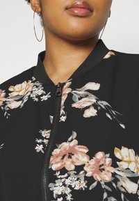 Svart bomberjacka med blommönster i rosa, krämfärg och grönt. Har dragkedja fram, ribbad krage och mjuk textur.
