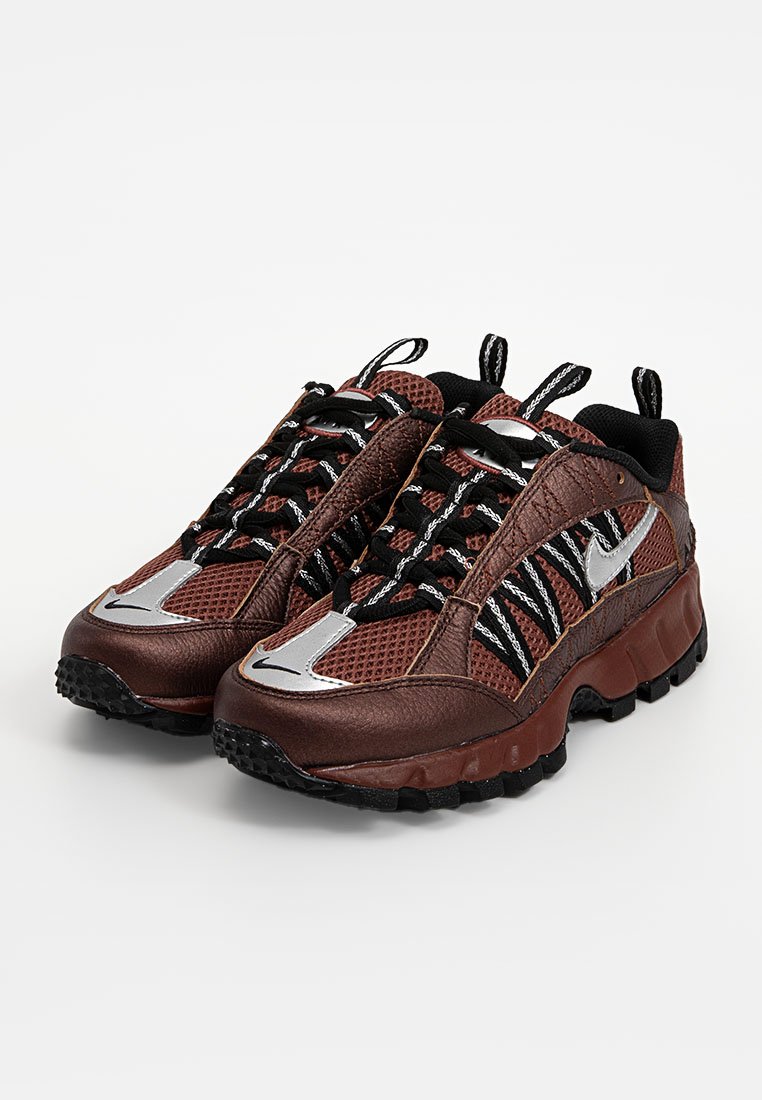 Baskets de sport marron et grises en mesh et cuir, avec des lacets noirs bien visibles, des accents argentés et une semelle en caoutchouc texturée.