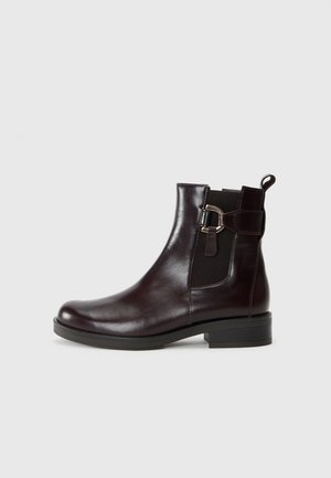 Bottine en cuir marron avec une finition lisse, des panneaux latéraux élastiques et un détail de boucle décoratif sur le côté extérieur. Talon bas.