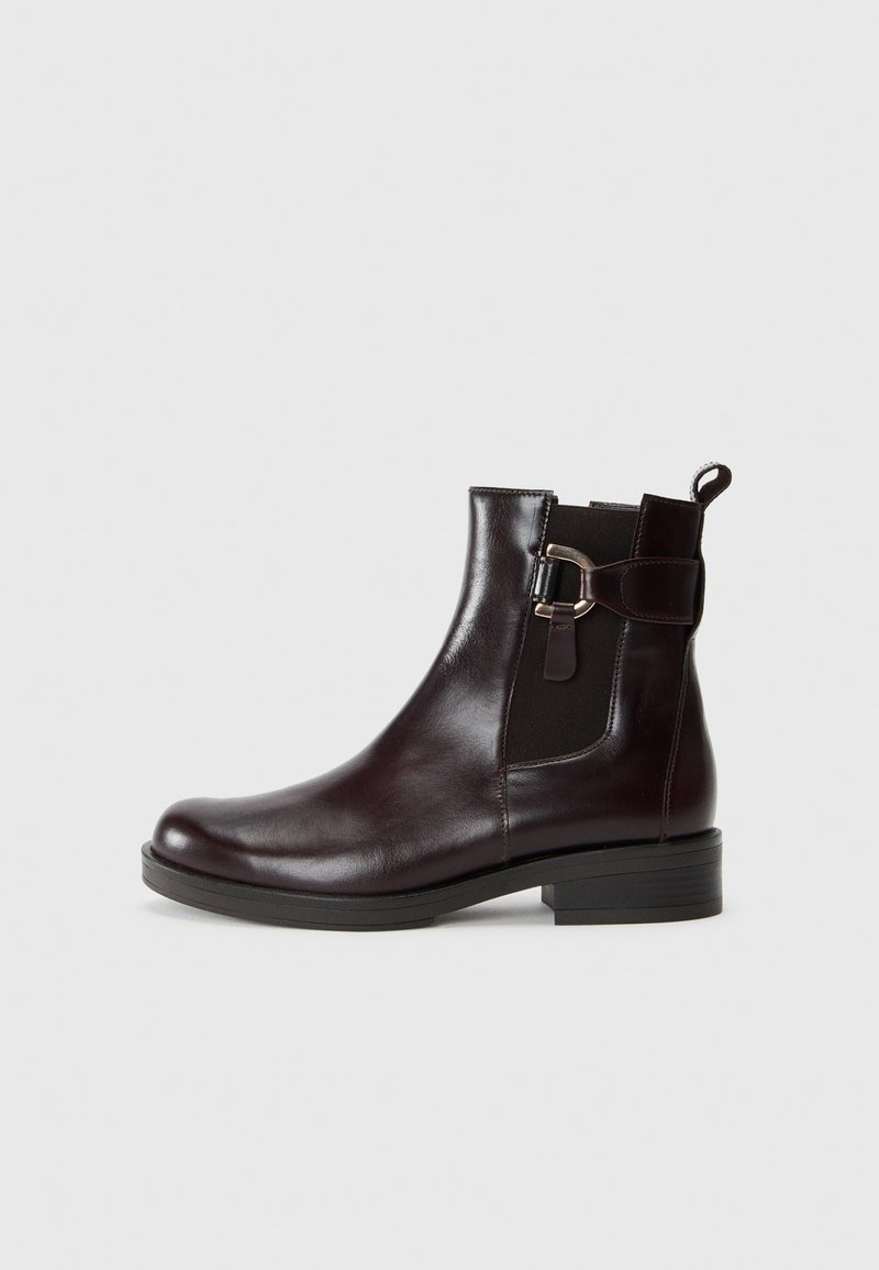 Bottine en cuir marron avec une finition lisse, des panneaux latéraux élastiques et un détail de boucle décoratif sur le côté extérieur. Talon bas.