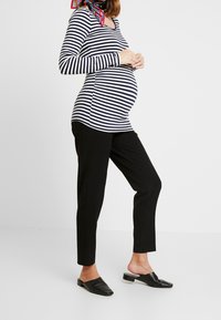 Randig långärmad topp i marinblått och vitt, tillsammans med svarta byxor. Svarta slip-on skor med ett strukturerat mönster kompletterar outfiten.