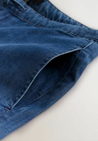 Dzemdžinsa auduma džinsi vidēji zilā krāsā ar maigu tekstūru, standarta kabatu dizainu un tīru šuvumu gar malām.