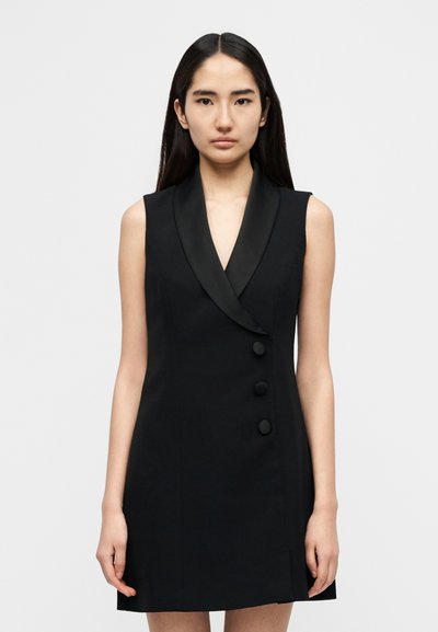 Fekete, ujjatlan ruha sallanggallérral, három elülső gombbal és testhez álló fazonnal. Simaszövet, minimális dizájnelemekkel.