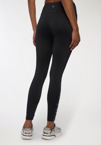 Czarne legginsy z wysokim stanem, z teksturowanym wzorem bocznych paneli. Noszone z szarymi butami sportowymi. Gładka faktura materiału.