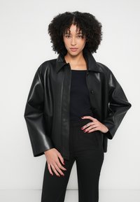 Czarna skórzana kurtka z zapięciem na guziki, dużym kołnierzem i lekko oversize'owymi rękawami, w zestawie z czarną bluzką i spodniami.