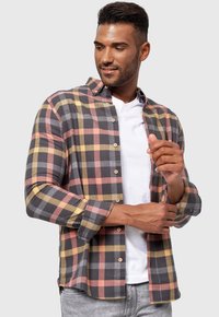 Camisa de cuadros con cuadrados grises, rosas y amarillos, diseño de botones, mangas enrolladas y un corte casual sobre una camiseta blanca.