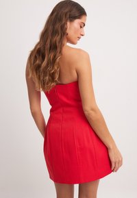Robe mini rouge sans bretelles avec un bodice ajusté et des détails de couture, dotée d'une fermeture éclair à l'arrière et d'un tissu lisse et texturé.