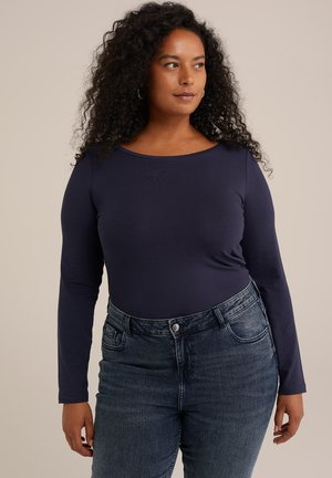 Marineblauwe longsleeve top van zacht materiaal, gecombineerd met donkerdenim jeans met middelhoog kruis, voorzien van zakken en een knoopsluiting.