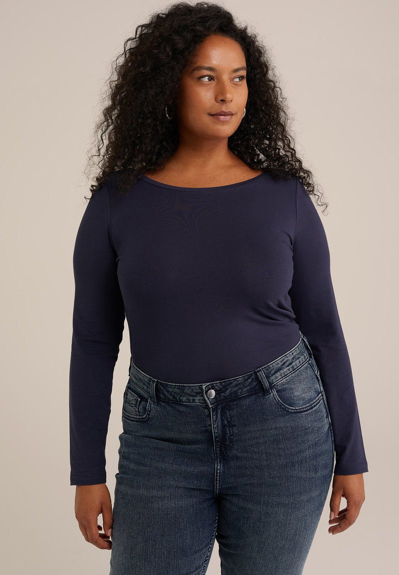 Top de manga larga azul marino, hecho de una tela suave, combinado con jeans oscuros de corte medio con bolsillos y cierre de botón.
