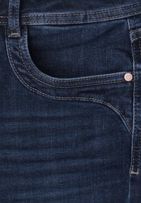 Gros plan d'une poche de jean en denim bleu foncé avec des coutures visibles et un petit rivet métallique sur le côté.