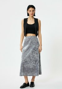Sort cropped vest over en grå velvet maxi nederdel med et tekstureret mønster, der har en elastisk talje og blanke sorte sko.