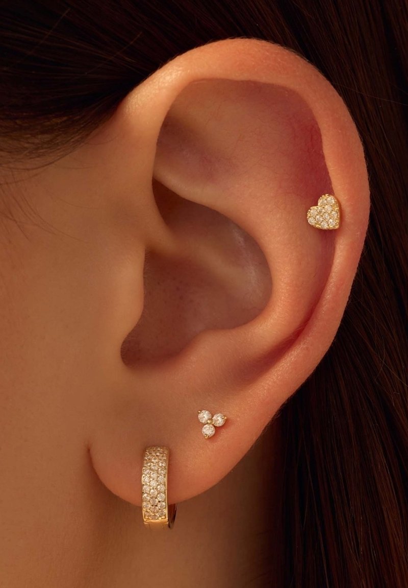 Boucle d'oreille en or avec des strass incrustés, un petit clou en or en forme de cœur, et un groupe de trois petits bijoux clairs, présentés sur une oreille.