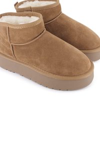 Botas de tobillo de ante marrón con un forro suave y esponjoso y suela de goma. Presentan una puntera redondeada y un diseño minimalista.