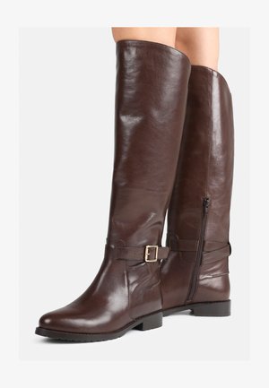 Hnedé kožené čižmy po kolená s hladkým povrchom, plochou podrážkou a bočným zipsom. Obsahujú tiež opasok so sponou pre pridanie detailu.