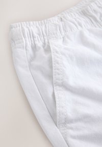 Primo piano di pantaloncini con fascia elastica bianca, che mostrano una tasca laterale e cuciture dettagliate su tessuto morbido.