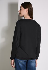 Maglietta nera a maniche lunghe con scollatura rotonda, texture morbida e orlo elastico, abbinata a jeans in denim blu visibili sotto.