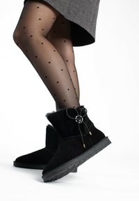 Botas de tobillo de ante negro con forro de felpa, puntera redondeada y cordones decorativos con detalles metálicos. Las medias de lunares añaden contraste.