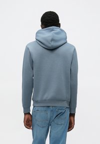 Lyseblå hættetrøje lavet af blødt bomuldsblanding, med rummelig hætte, ribstrikkede manchetter og kant, båret sammen med lyseblå jeans.