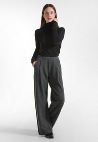 Schwarzer Rollkragenpullover kombiniert mit hochgeschnittenen, weit geschnittenen grauen Hosen, die ein dezentes Streifenmuster und Seitentaschen aufweisen.