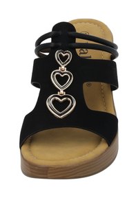 Sandale noire à talon plat avec trois accents en forme de cœurs entrelacés en métal doré, dotée d'une semelle intérieure rembourrée et d'une semelle à texture bois.