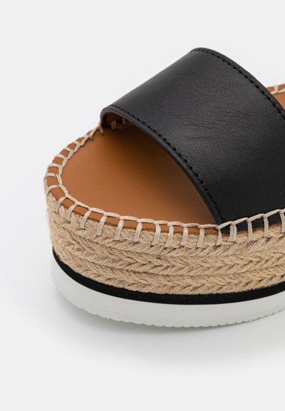 Sorte skinn slidesandal med en flettet juteplattform, lys brun fotseng og hvit gummisåle med en svart stripe.