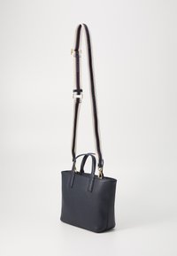 Sac à main en cuir bleu marine avec une forme structurée, deux poignées supérieures et une bandoulière rayée amovible avec des accents rouges et blancs.